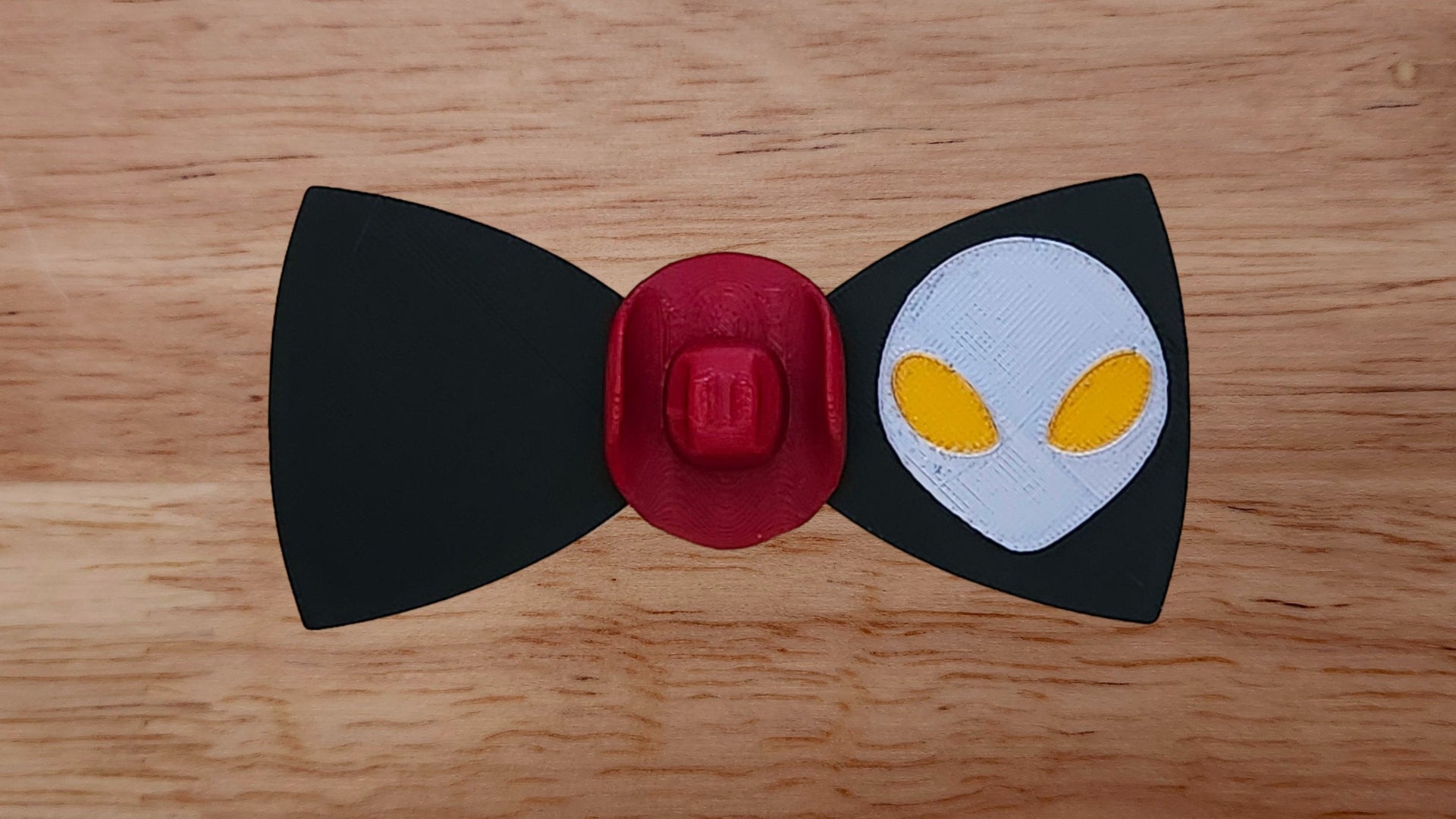 Red cowboy hat base in center with black bow tie featuring silver alien head back on wooden background. 