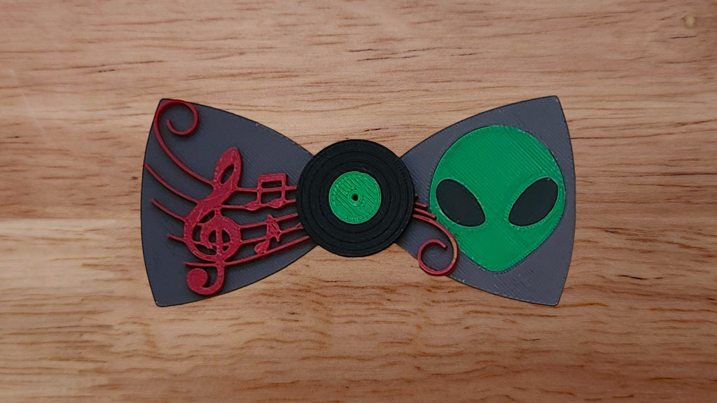 Vinyl record base in center with green alien head back and red sheet music bow tie on wooden background. 