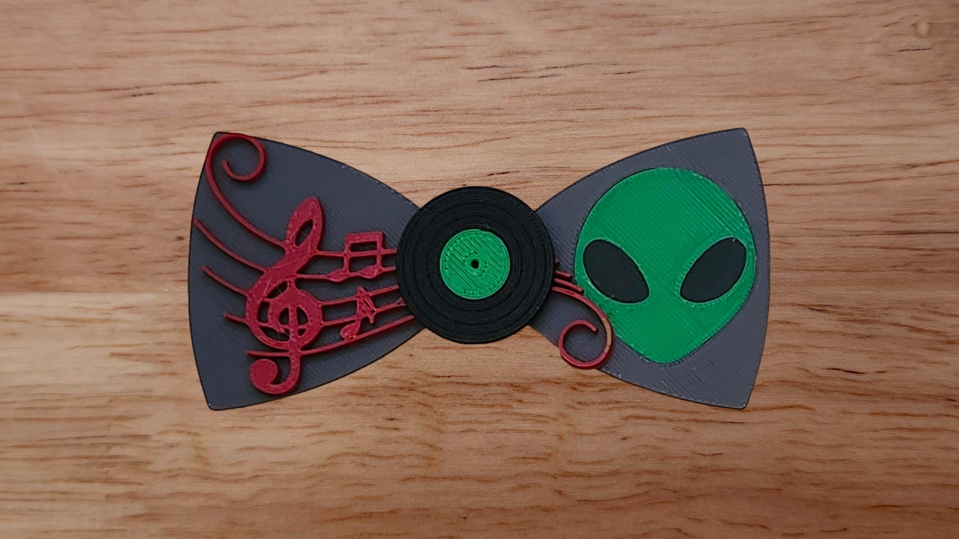 Vinyl record base in center with green alien head back and red sheet music bow tie on wooden background. 