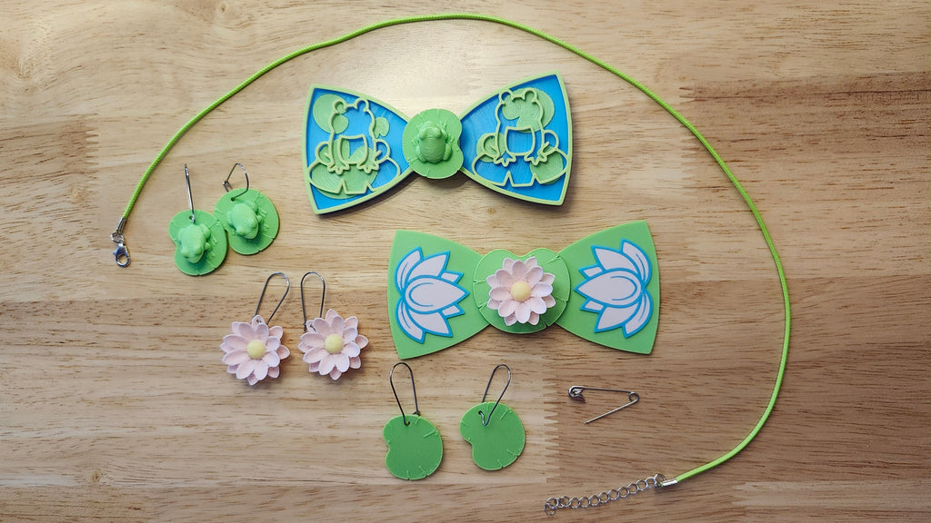 Lily Pond Bow Big Bundle including Frog Button Cover, Lily Pad Bow, Frog Outline Bow, the Lotus Flower Button Cover, Lotus Bow, Lily Pad Back, matching Frog on Lily Pad, Lotus Flower and Lily Pad earrings, 2 safety pins and silvery necklace. 3D printed for use as a bow tie, button cover, necklace, pin, hat pin, lapel pin and so much more. 