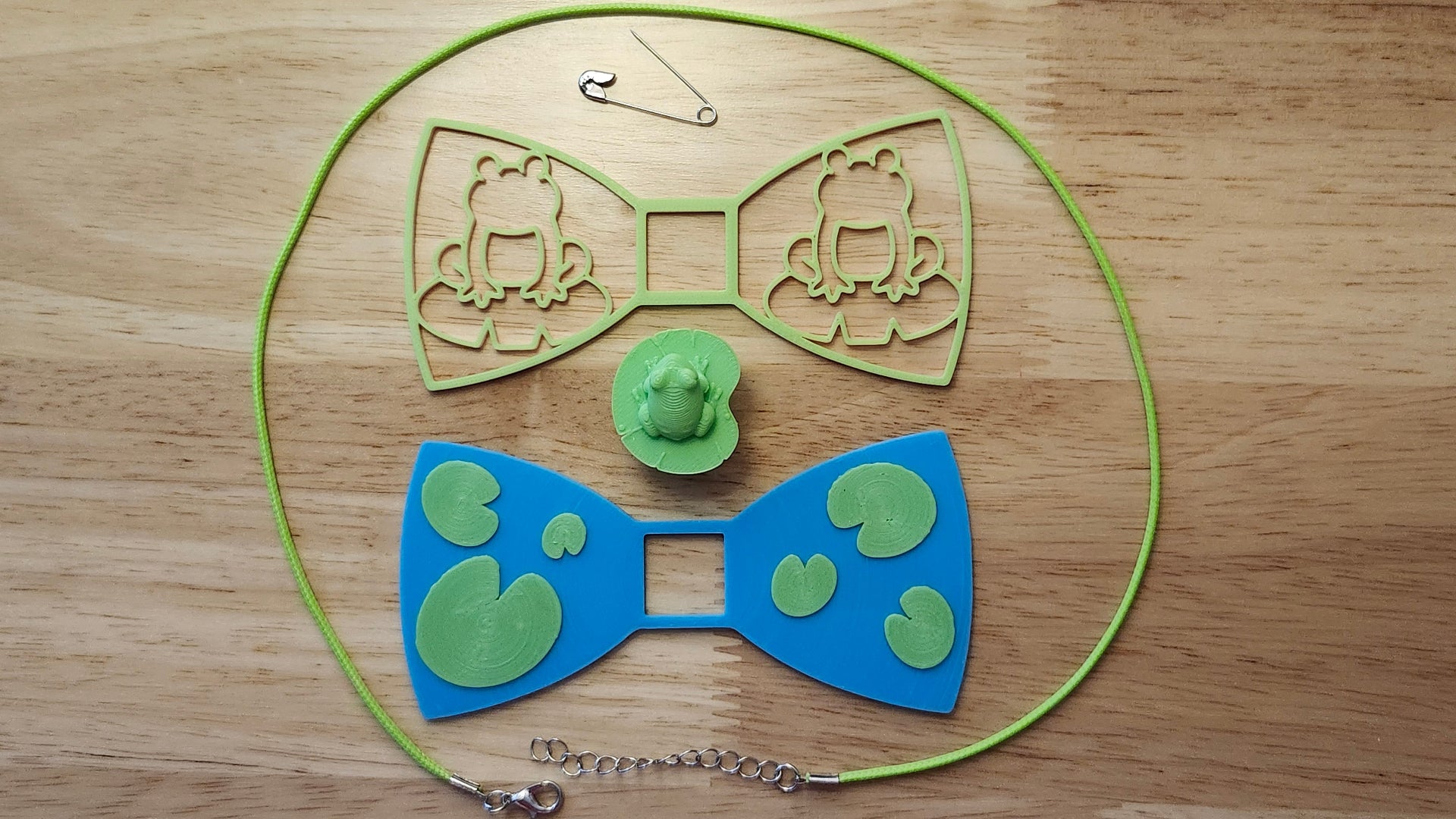 Frog Bow Bundle including Frog Button Cover, Lily Pad Bow, Frog Outline Bow, a safety pin and silvery necklace. 3D printed for use as a bow tie, button cover, necklace, pin, hat pin, lapel pin and so much more. 