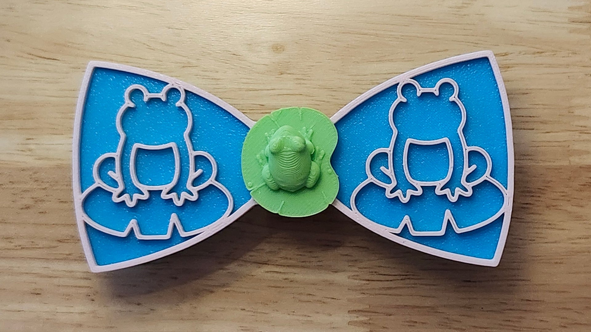 Frog Button Cover with Lily Pad Bow (reverse side shown), Frog Outline Bow (pink side). 3D printed for use as a bow tie, button cover, necklace, pin, hat pin, lapel pin and so much more. 