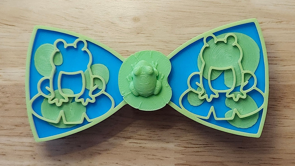 Frog Button Cover with Lily Pad Bow, Frog Outline Bow (green side). 3D printed for use as a bow tie, button cover, necklace, pin, hat pin, lapel pin and so much more. 