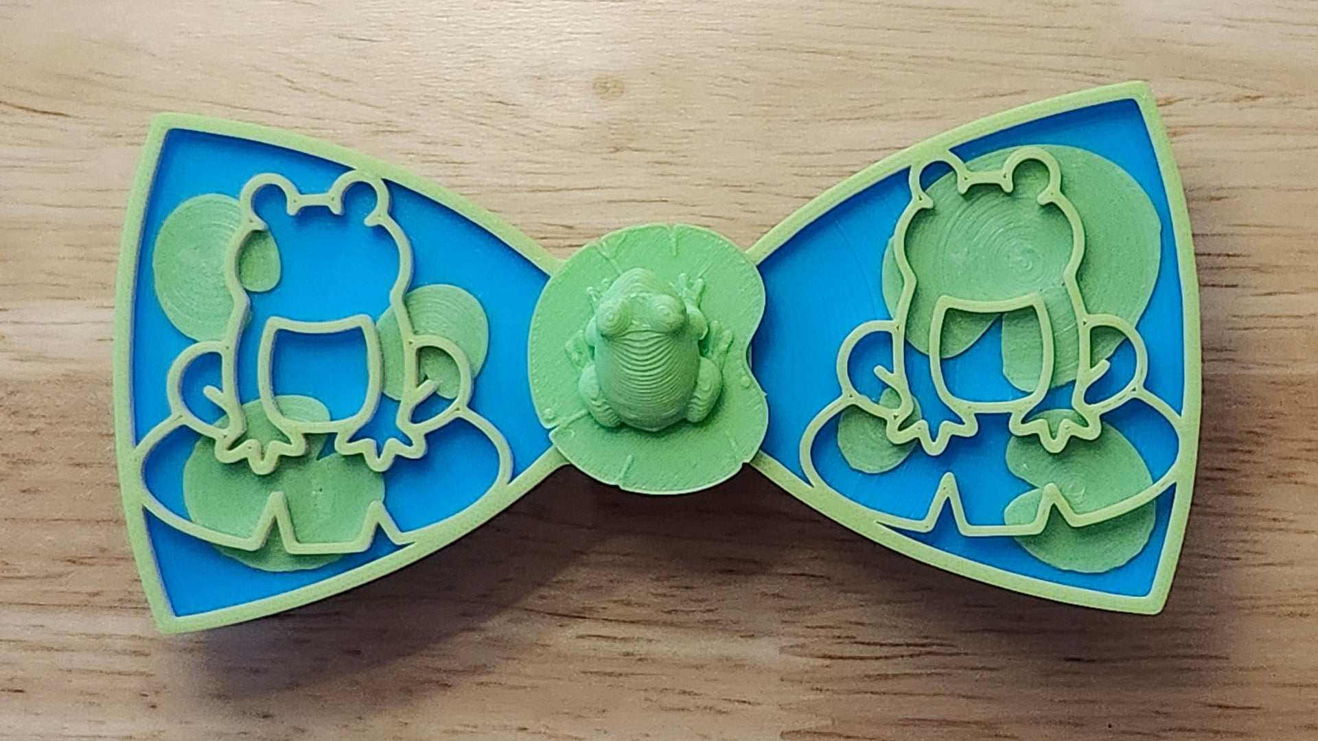 Frog Button Cover with Lily Pad Bow, Frog Outline Bow (green side). 3D printed for use as a bow tie, button cover, necklace, pin, hat pin, lapel pin and so much more. 