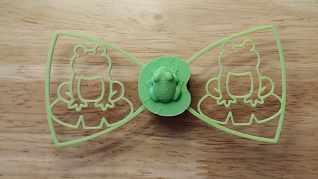 Frog Button Cover with Frog Outline Bow (green side). 3D printed for use as a bow tie, button cover, necklace, pin, hat pin, lapel pin and so much more. 