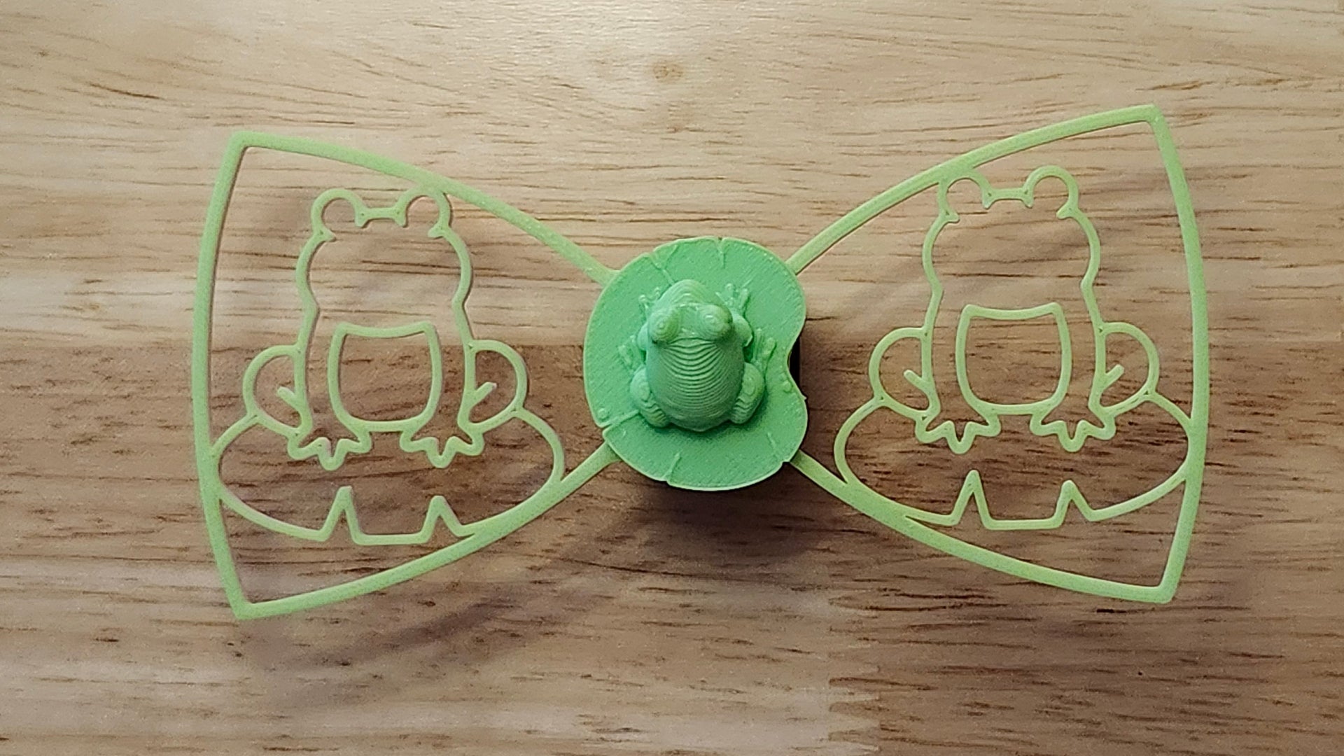 Frog Button Cover with Frog Outline Bow (green side). 3D printed for use as a bow tie, button cover, necklace, pin, hat pin, lapel pin and so much more. 