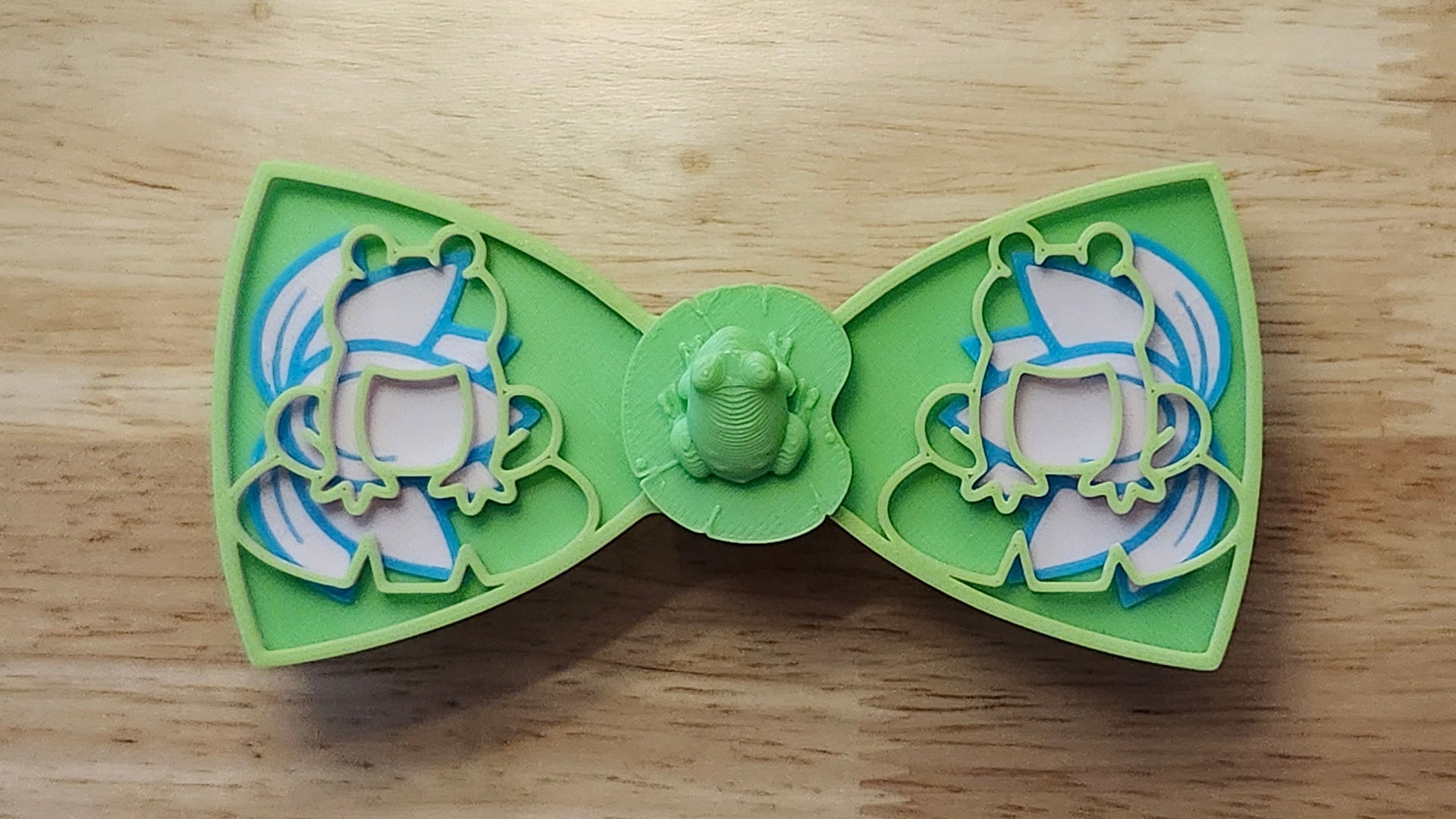 Frog Button Cover with Frog Outline Bow (green side) and Lotus Bow. 3D printed for use as a bow tie, button cover, necklace, pin, hat pin, lapel pin and so much more. 