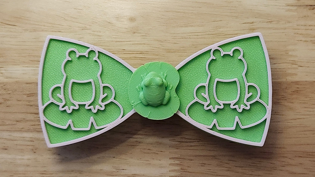 Frog Button Cover with Frog Outline Bow (pink side) and Lotus Bow (reverse side). 3D printed for use as a bow tie, button cover, necklace, pin, hat pin, lapel pin and so much more. 