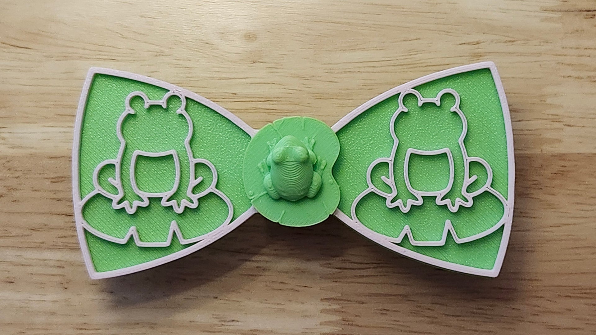 Frog Button Cover with Frog Outline Bow (pink side) and Lotus Bow (reverse side). 3D printed for use as a bow tie, button cover, necklace, pin, hat pin, lapel pin and so much more. 