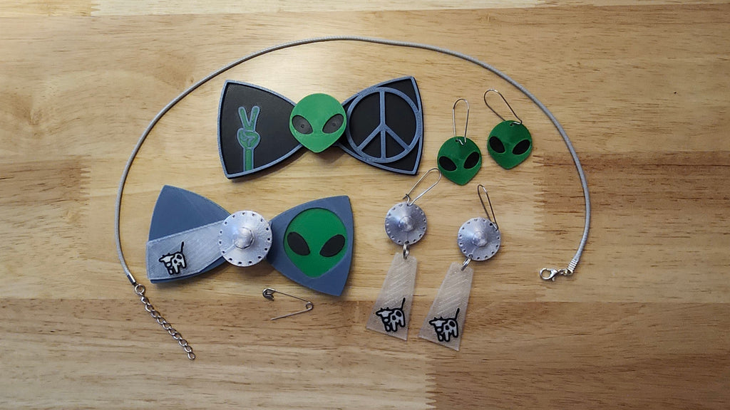 Aliens Are Real Bow Big Bundle including UFO Button Cover, Alien Head Bow, Cow Beaming Back, Alien Head Button Cover, Alien Peace Hand Bow, Peace Sign Bow, matching UFO Beaming Up Cow and Alien Head earrings 2 safety pins and an 18 inch gray necklace. 3D printed for use as a bow tie, button cover, necklace, pin, hat pin, lapel pin and so much more. 