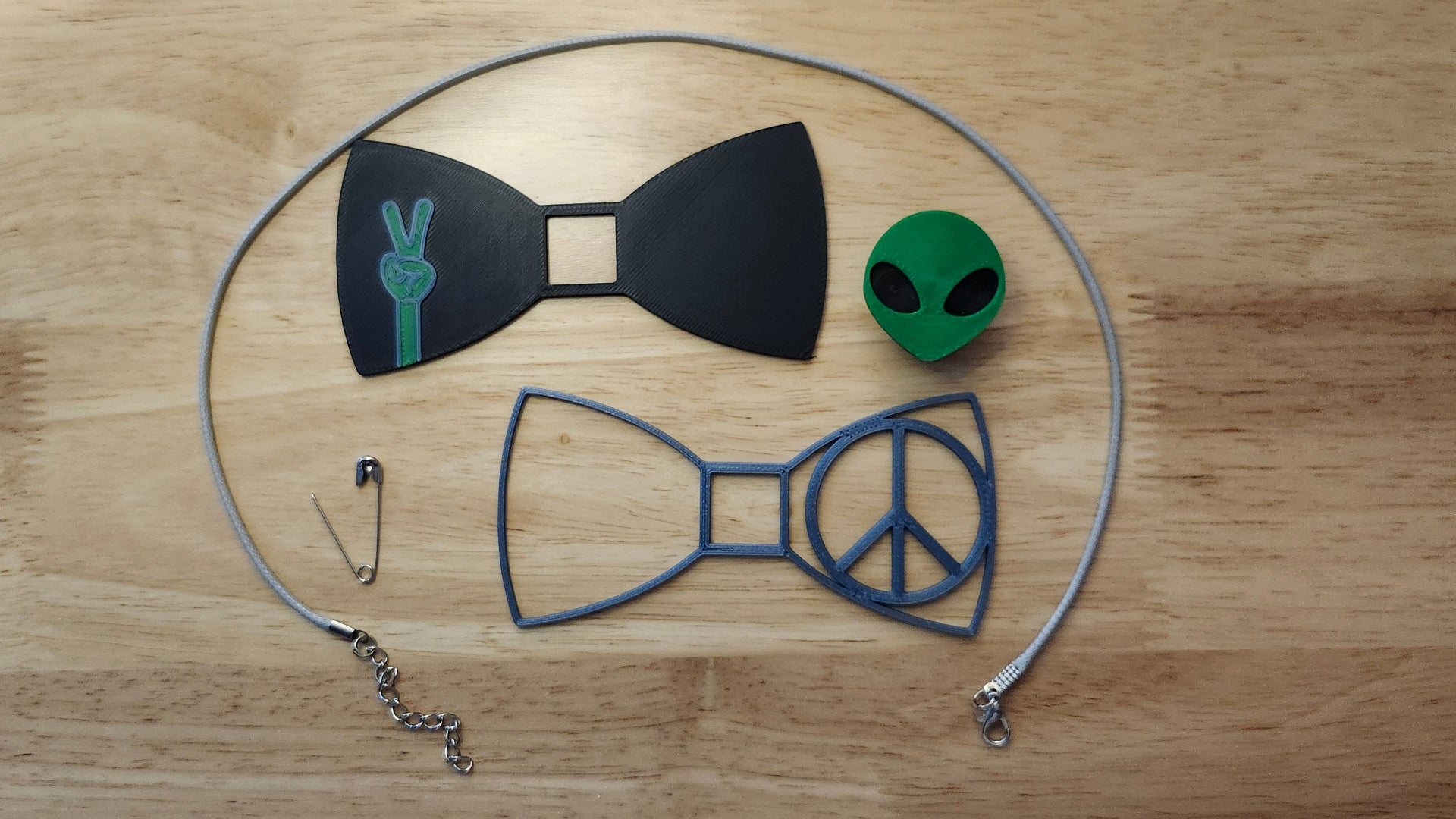 They Come In Peace Bow Bundle including Alien Head Button Cover, Alien Peace Hand Bow, Peace Sign Bow, a safety pin and an 18 inch gray necklace. 3D printed for use as a bow tie, button cover, necklace, pin, hat pin, lapel pin and so much more. 