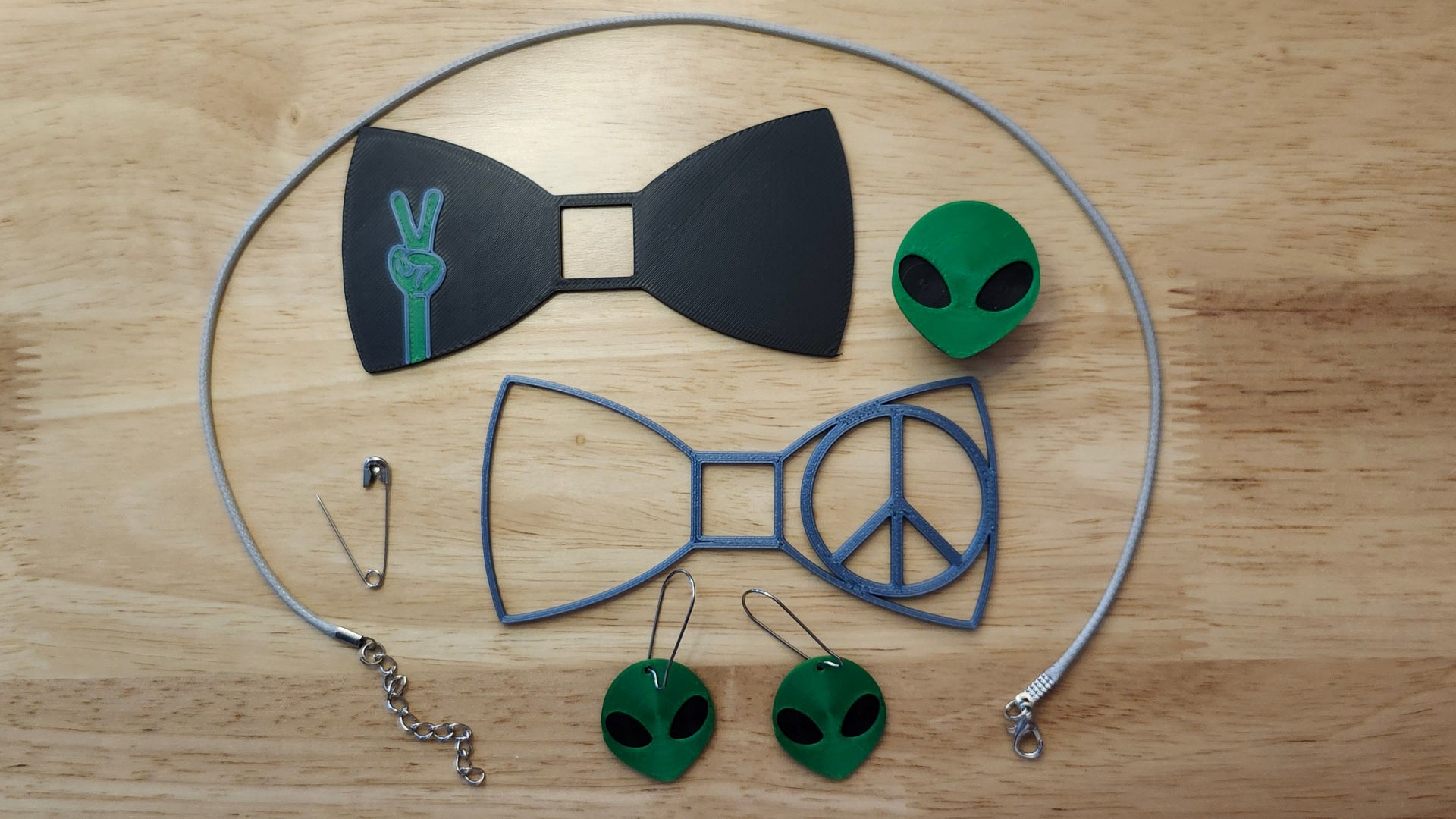 They Come In Peace Bow Bundle including Alien Head Button Cover, Alien Peace Hand Bow, Peace Sign Bow, matching Alien Head earrings, a safety pin and an 18 inch gray necklace. 3D printed for use as a bow tie, button cover, necklace, pin, hat pin, lapel pin and so much more. 