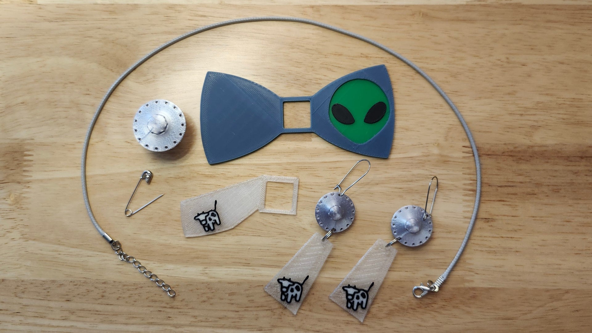 UFO Bow Bundle including UFO Button Cover, Alien Head Bow, Cow Beaming Back, matching UFO Beaming Up Cow earrings, a safety pin and an 18 inch gray necklace. 3D printed for use as a bow tie, button cover, necklace, pin, hat pin, lapel pin and so much more. 