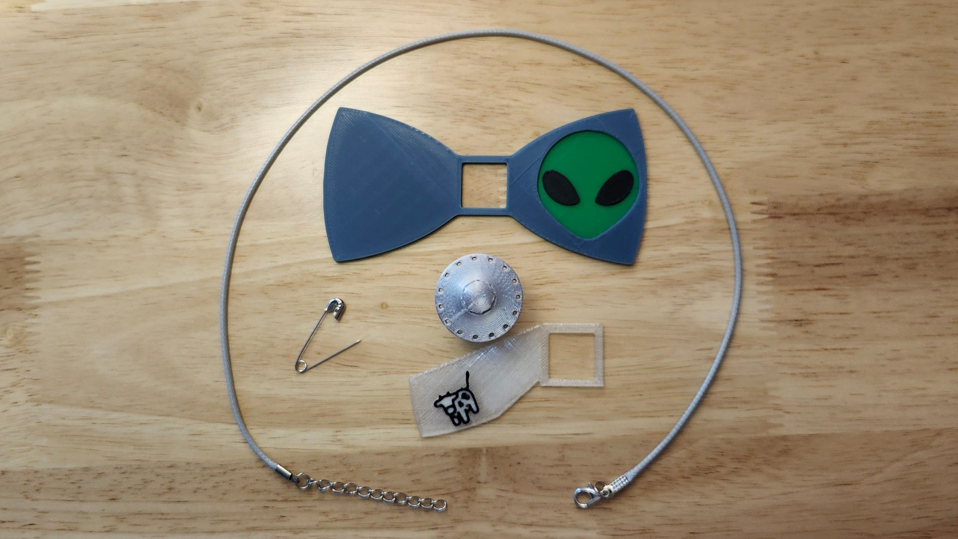 UFO Bow Bundle including UFO Button Cover, Alien Head Bow, Cow Beaming Back, a safety pin and an 18 inch gray necklace. 3D printed for use as a bow tie, button cover, necklace, pin, hat pin, lapel pin and so much more. 