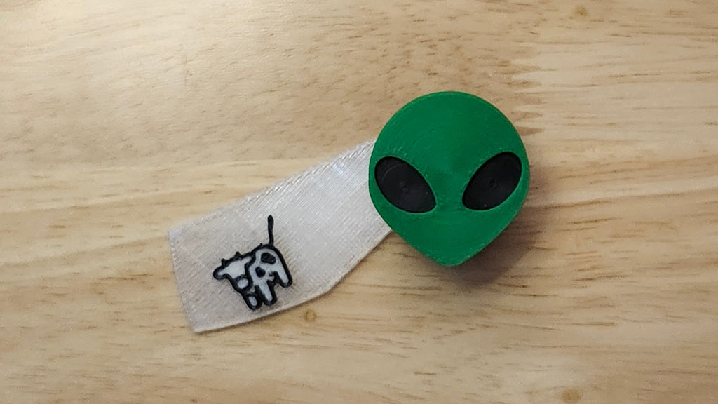 Alien Head Button Cover with Cow Beaming Back. 3D printed for use as a bow tie, button cover, necklace, pin, hat pin, lapel pin and so much more.