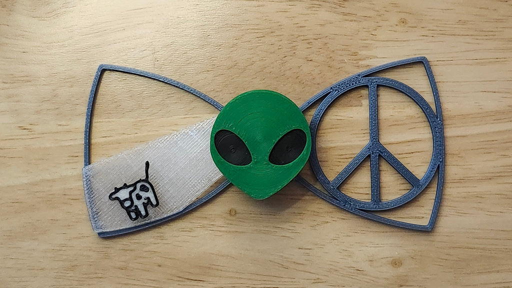 Alien Head Button Cover with Peace Sign Bow and Cow Beaming Back. 3D printed for use as a bow tie, button cover, necklace, pin, hat pin, lapel pin and so much more.